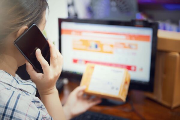 Passive Income from Dropshipping: The Ultimate Guide for 2025 Woman using smartphone while managing online orders on computer, representing e-commerce and customer suppor